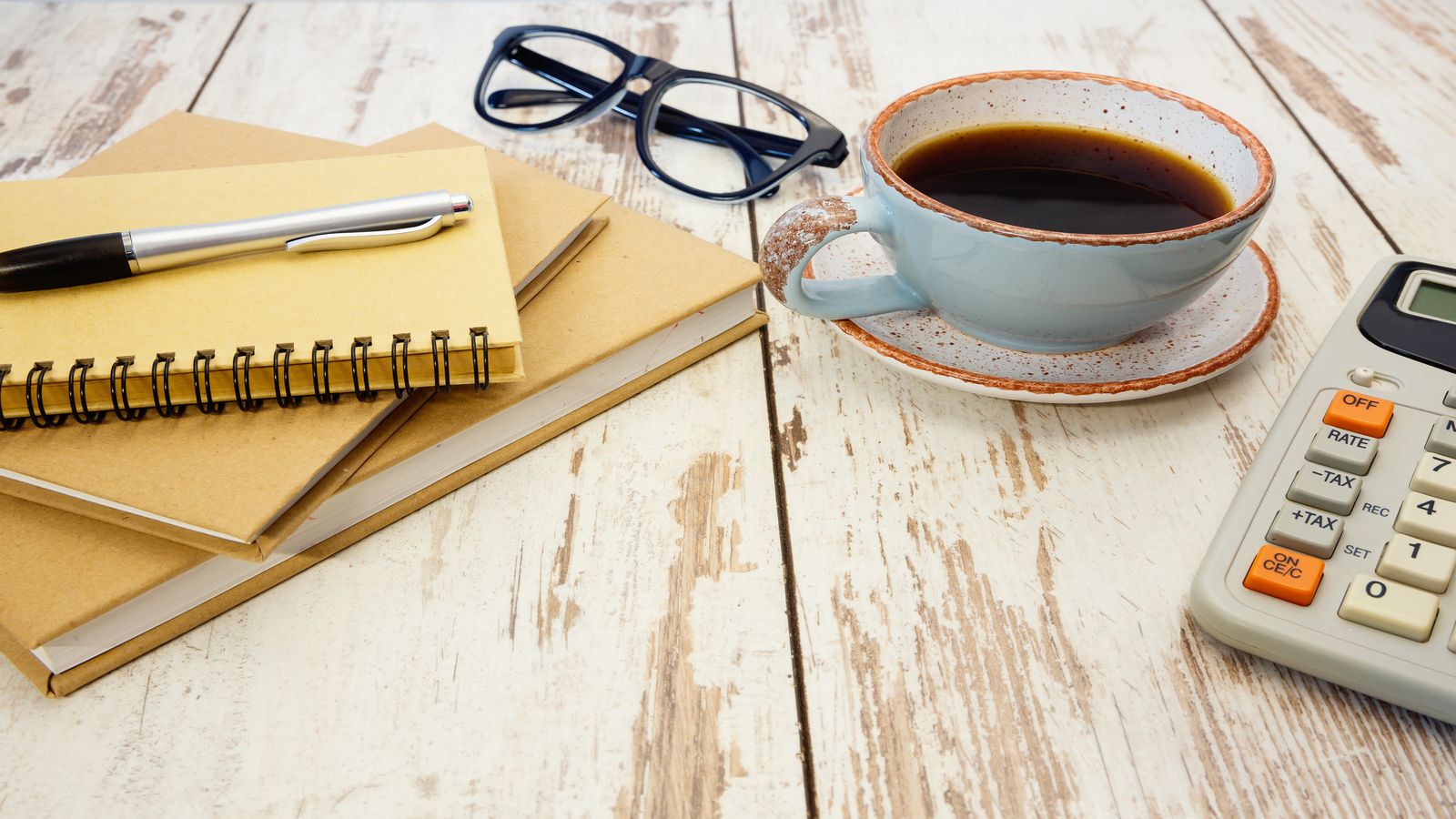Desk with a ledger book, a calculator, handwritten Bitcoin transaction records, and a cup of tea